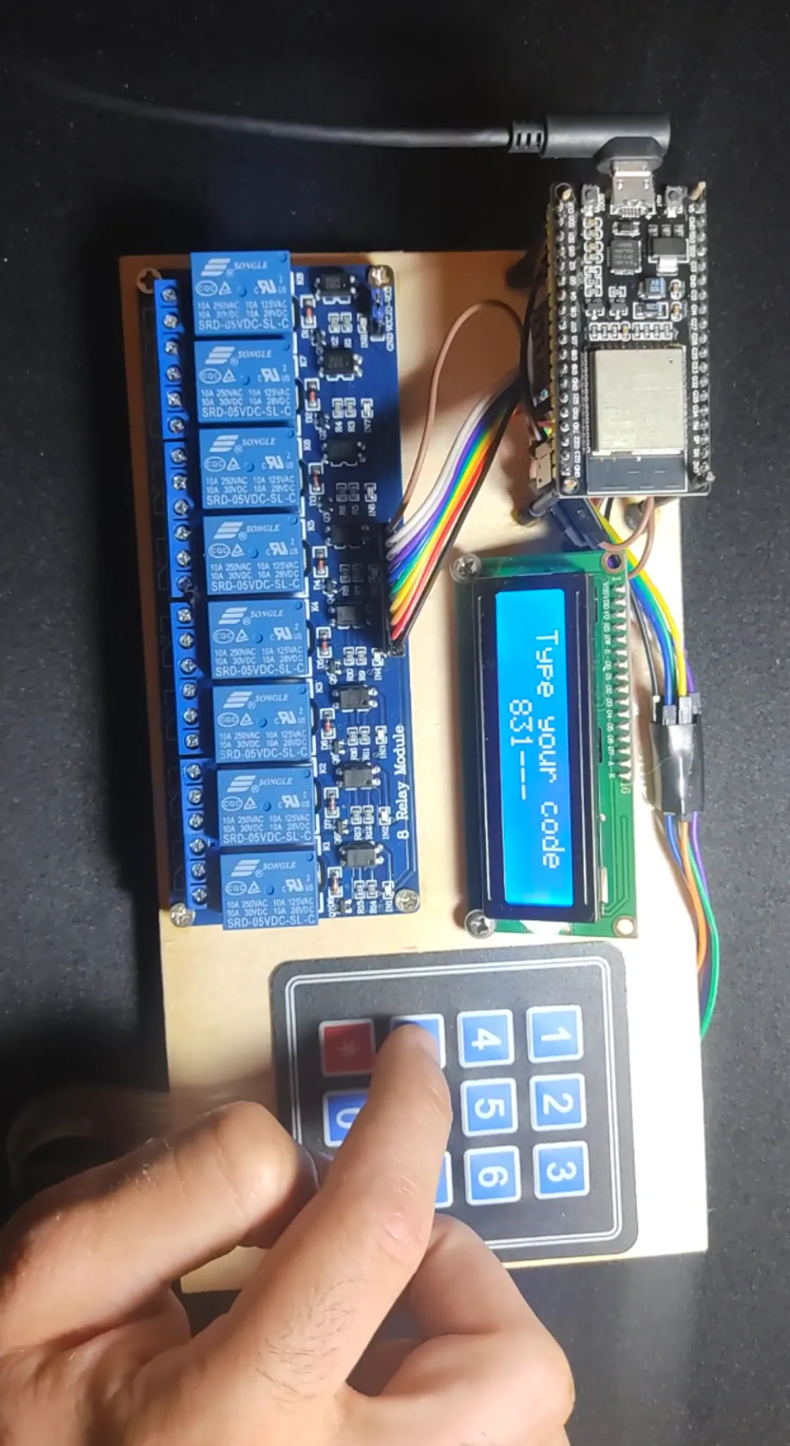 O controlador Gestire montado, com um ESP32, uma placa de oito relés, um LCD e uma mão a introduzir um código no teclado.